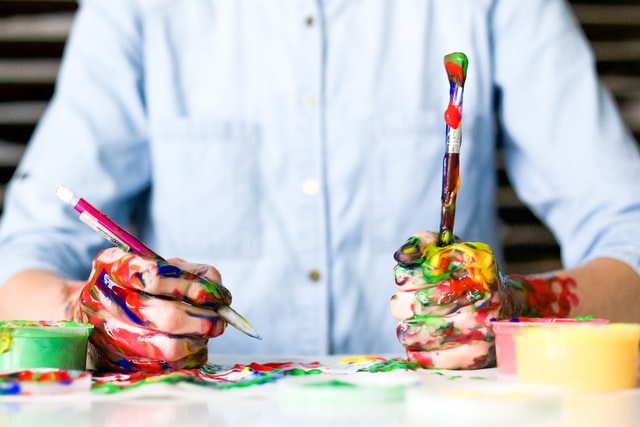 Djak sa olovkom u desnoj ruci a četkicom u levoj, umazan od boja po obe šake koje su oslonjene na hartiju za crtanje